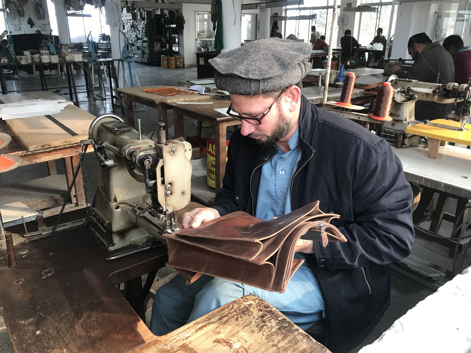 Ein Mitarbeiter näht eine braune Ledertasche an einer Maschine.