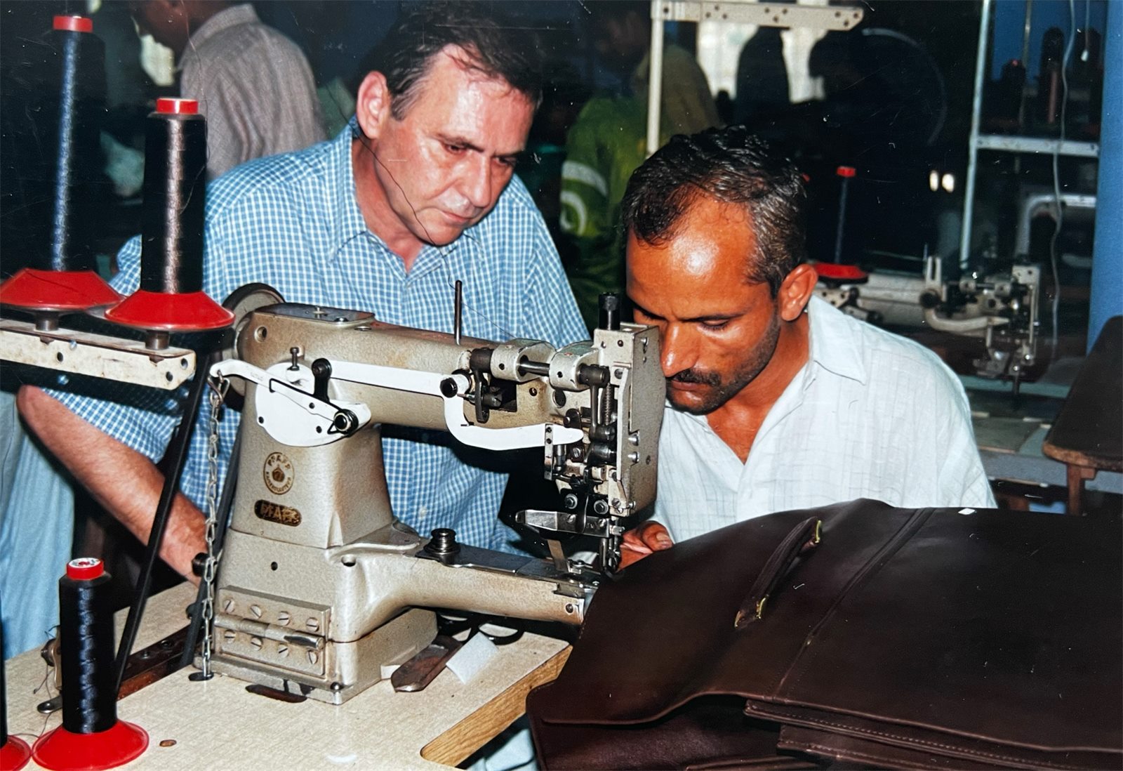 Zwei Männer arbeiten an einer Industrienähmaschine an einer Ledertasche.